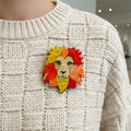 Acrylic lion head brooch featuring layered detailing pinned on a ivory sweater
