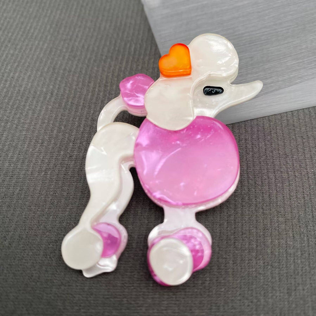 Pink and white poodle-shaped brooch on a gray background