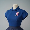 Pink and white poodle-shaped brooch pinned on a blue bouse