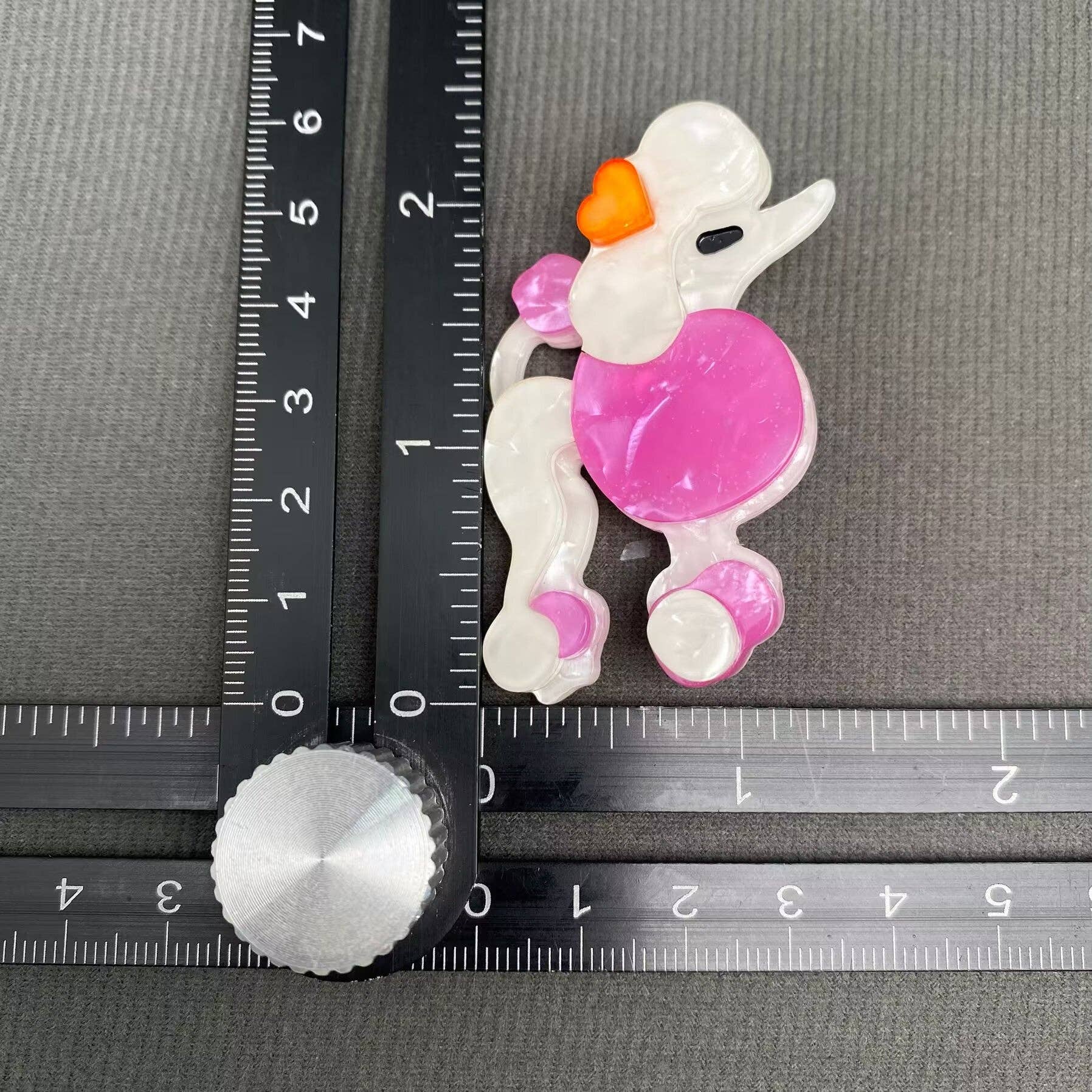 Pink and white poodle-shaped brooch on a gray background