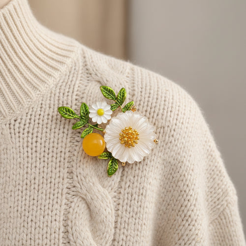 Floral brooch with white flowers, green leaves, and a yellow berry pinned on a white sweater