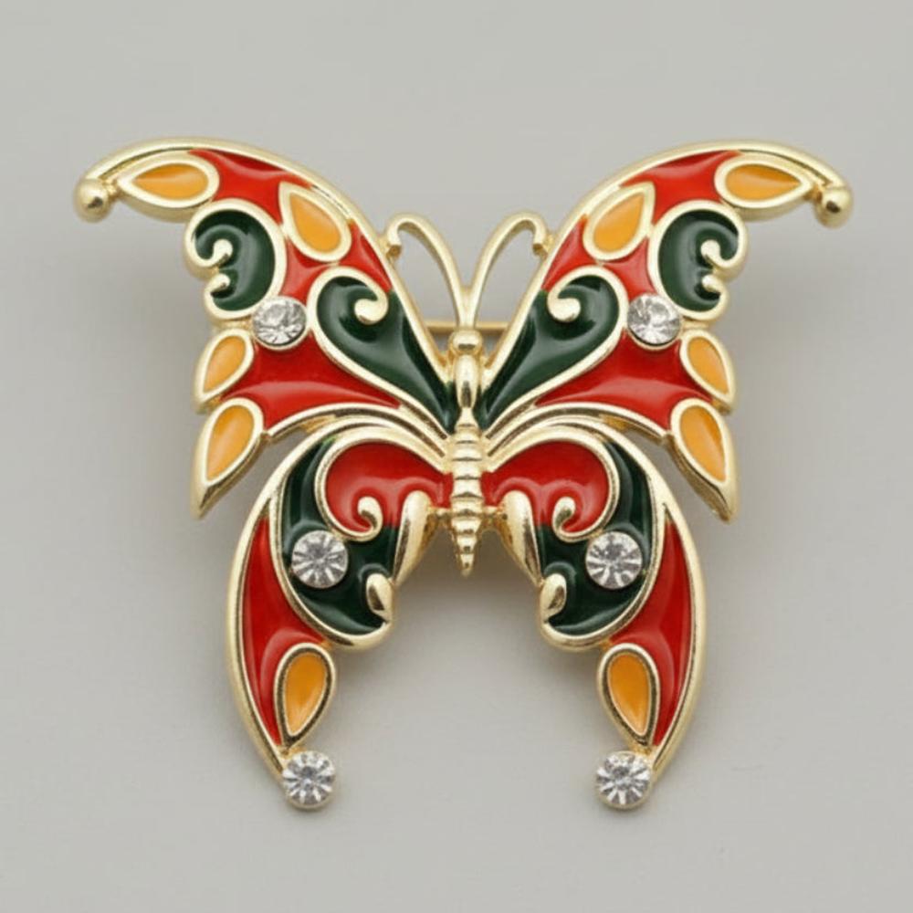 Butterfly-shaped brooch with red, green, and gold colors on a gray background