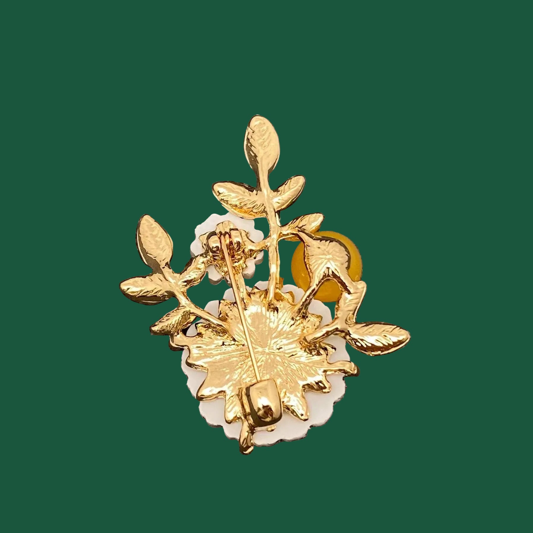 Back view of daisy brooch showing clasp and hinge mechanism on a green background