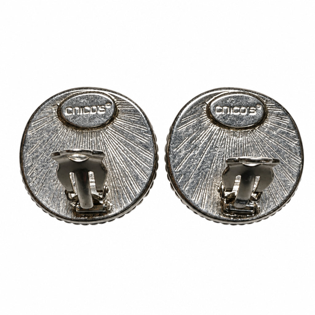 Back view of Chico's hallmarked pair of round silver-tone metal clip-on earrings with a textured sunburst pattern, shown on a light gray background.