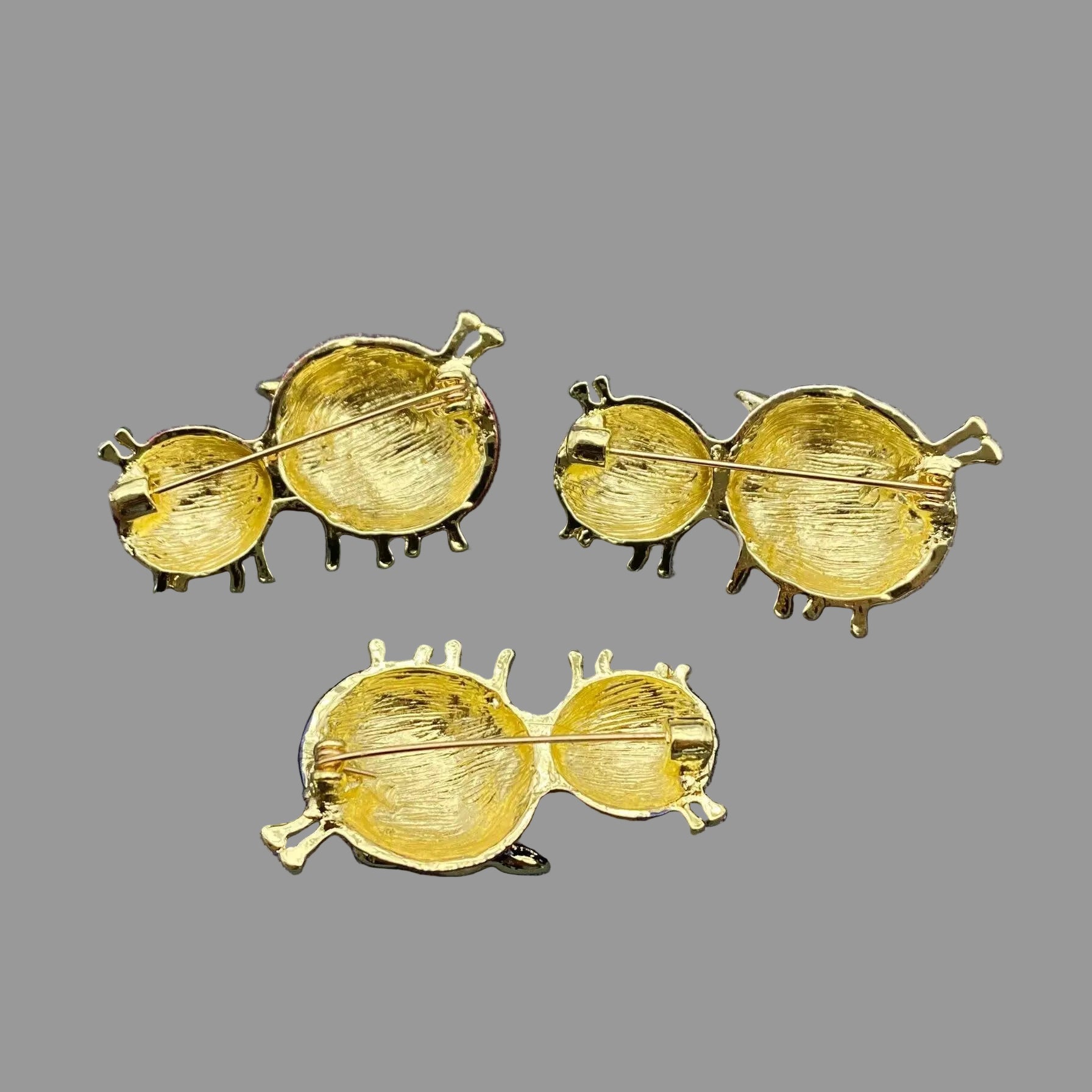 Back view of pair of sheep-shaped brooch pins showing the clasp mechanism, on a gray background