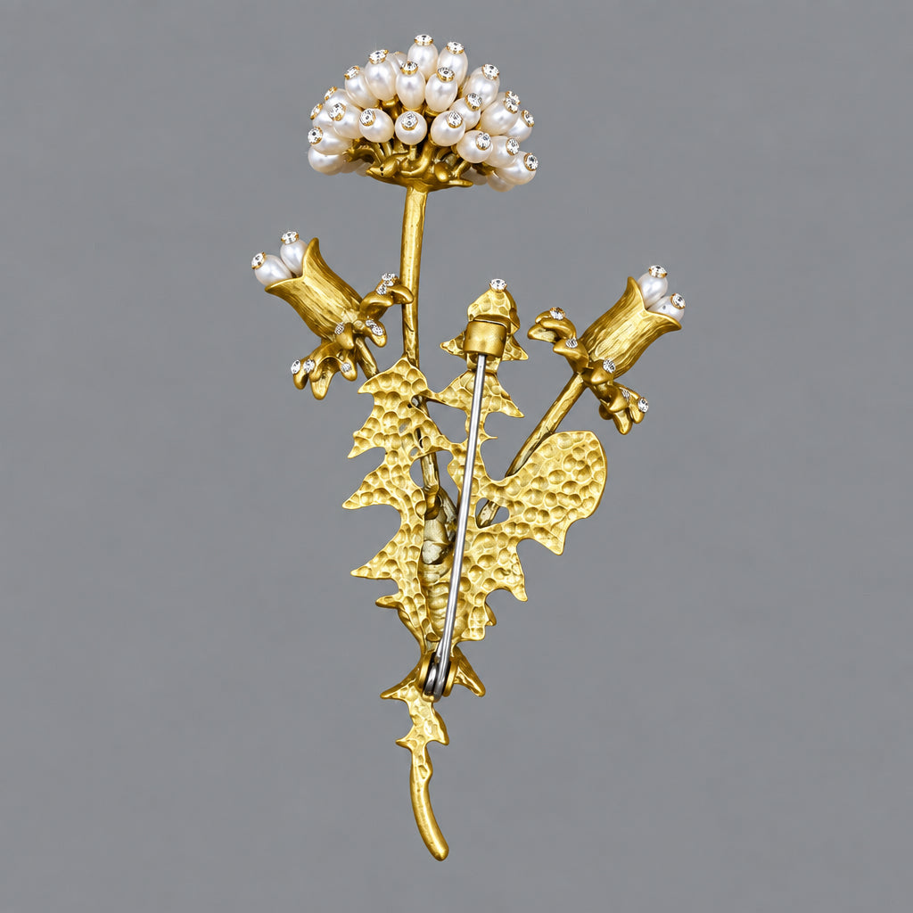 Back view of a dandelion brooch with white pearl-like blossoms and iridescent rhinestones, attached to metallic gold-green stems and leaves, showing the clasp mechanism.
