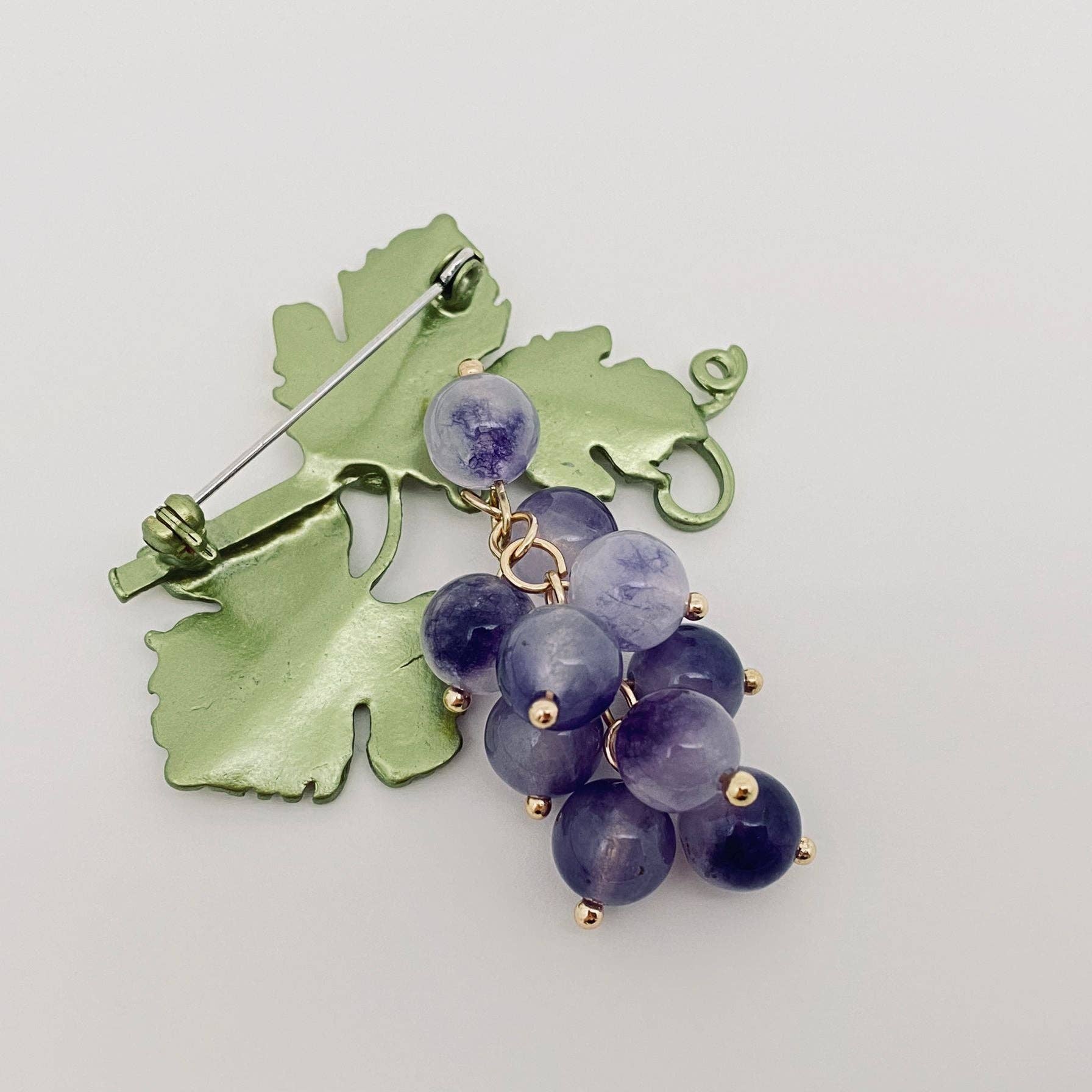 Back view of brooch with green leaf design and purple glass stones, showing the clasp mechanism