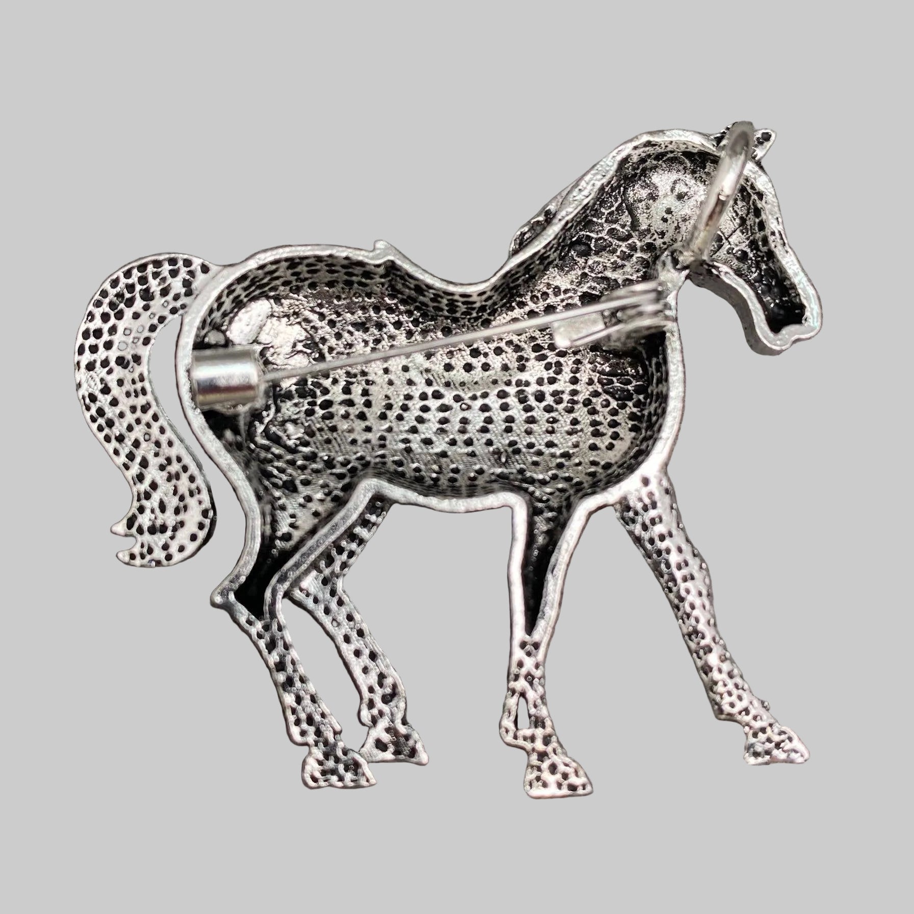 Back view of red horse-shaped brooch with blue saddle, showing the clasp mechanism