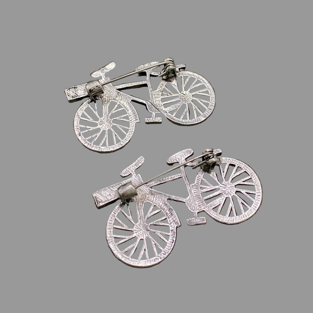 Back view of two bicycle shaped brooches, showing the clasp mechanism