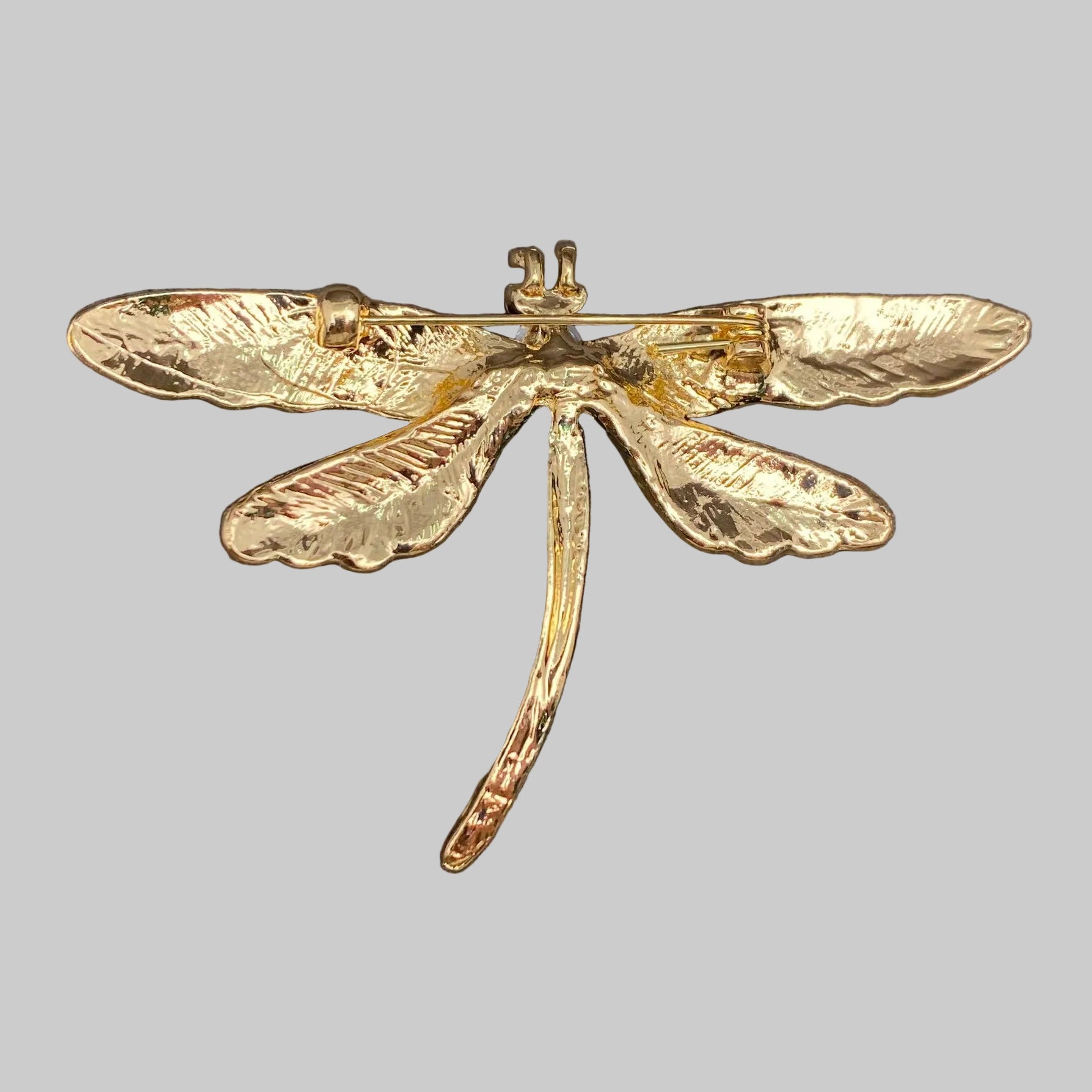 Back view of colorful dragonfly-shaped brooch showing the clasp mechanism, on a gray background