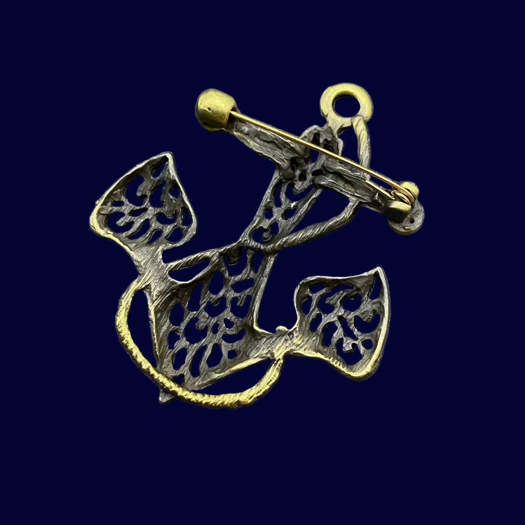 Back view of bronze anchor-shaped brooch showing the clasp mechanism on a blue background