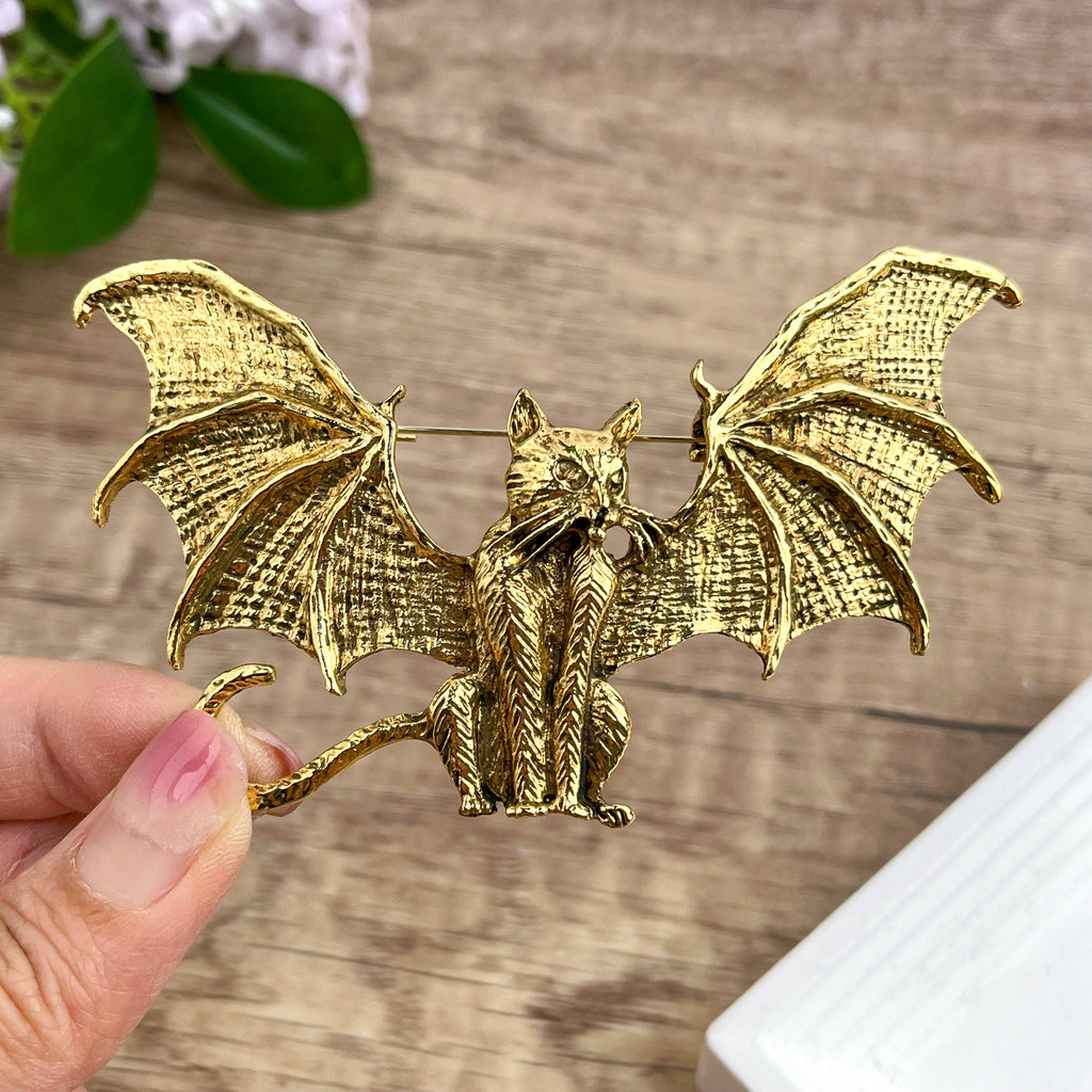 Gold metal bat-shaped brooch featuring a cat adorned with dimensional bat wings