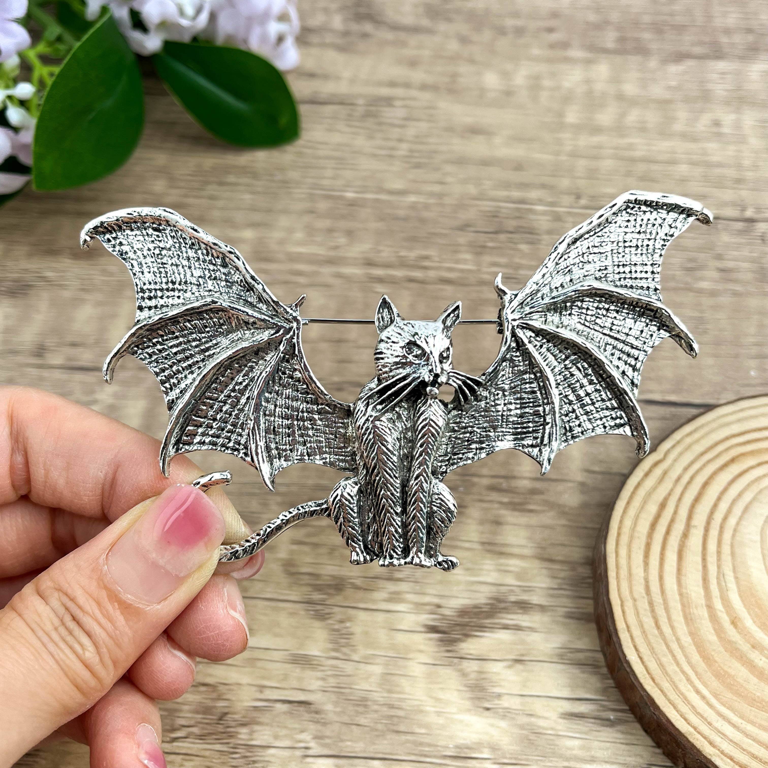 Silver metal bat-shaped brooch featuring a cat adorned with dimensional bat wings