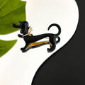 Black and gold dachshund-shaped brooch on a white background