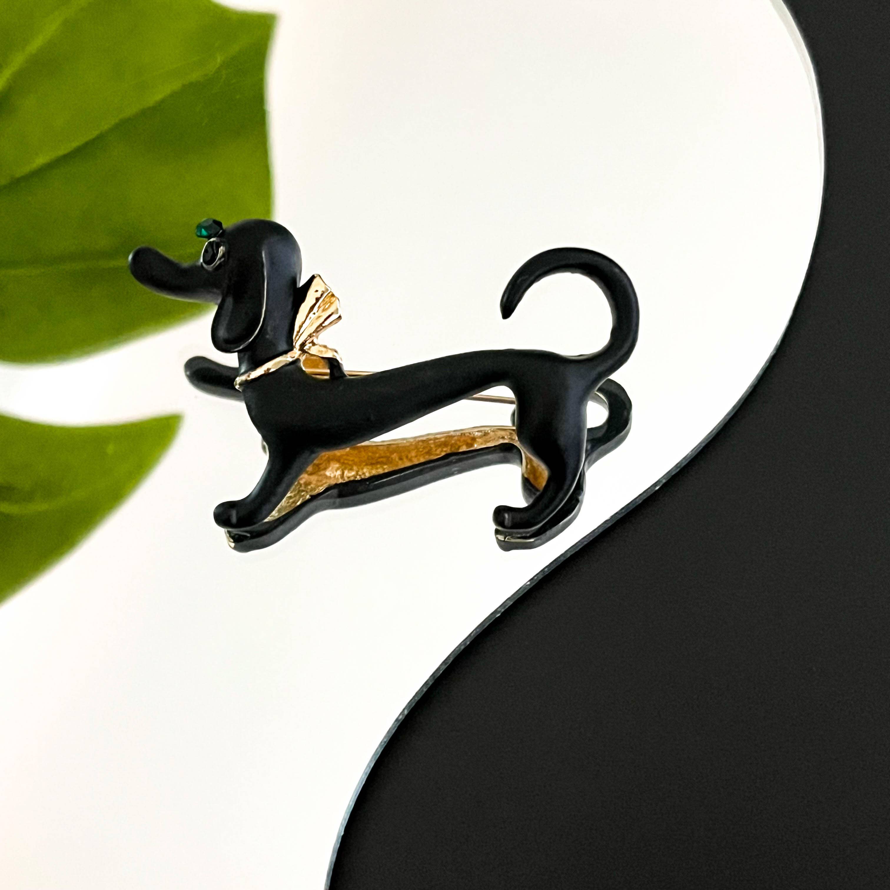 Black and gold dachshund-shaped brooch on a white background