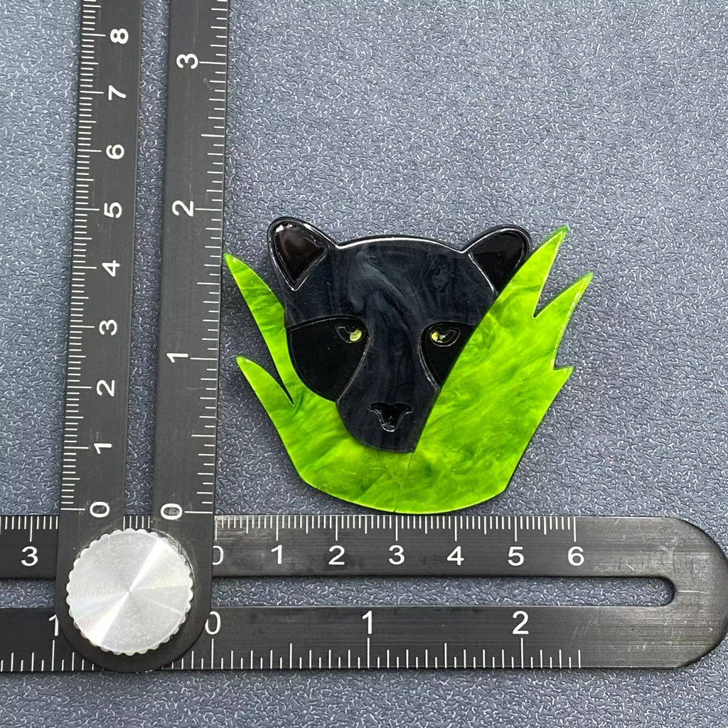 Black panther on green leaves brooch with a ruler for scale on a gray background