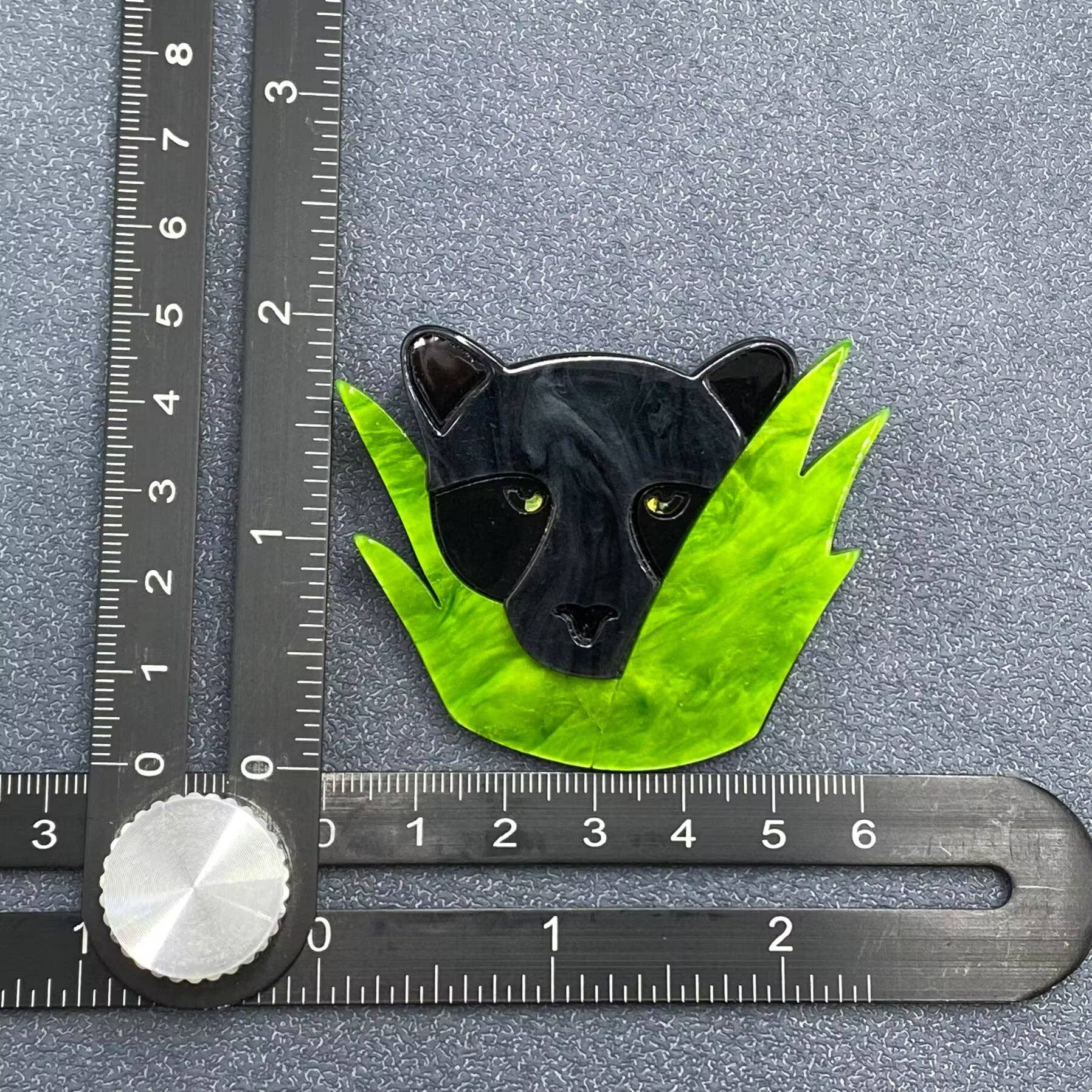 Black panther on green leaves brooch with a ruler for scale on a gray background