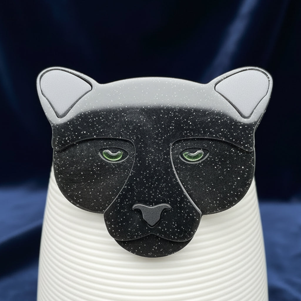 Black cat-shaped brooch on a white cylindrical container with a blue background