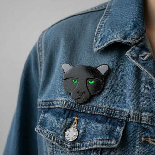 Black panther-shaped brooch with green eyes pinned on a denim jacket