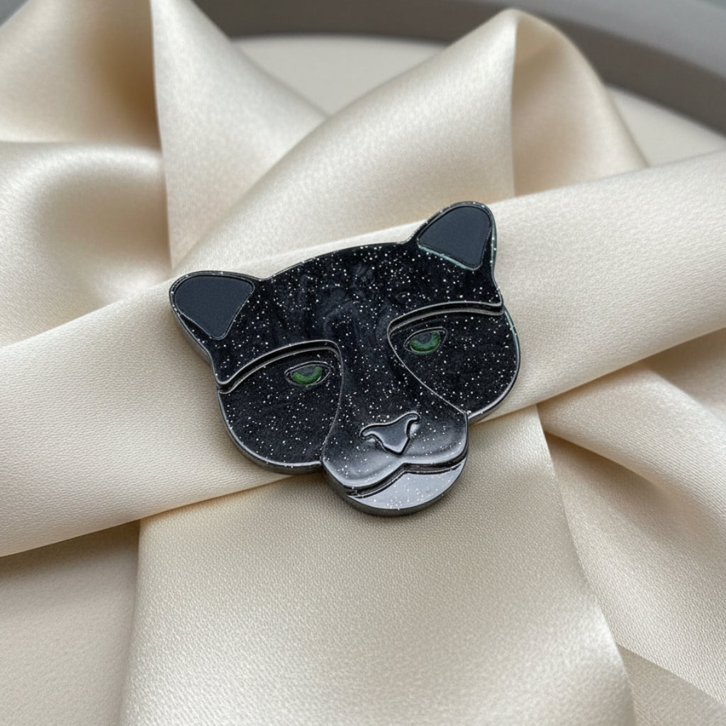 Black panther head-shaped brooch with green eyes on a ivory silk background