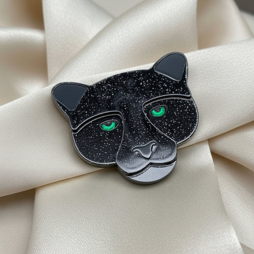 Black panther-shaped brooch with green eyes on a ivory silk background