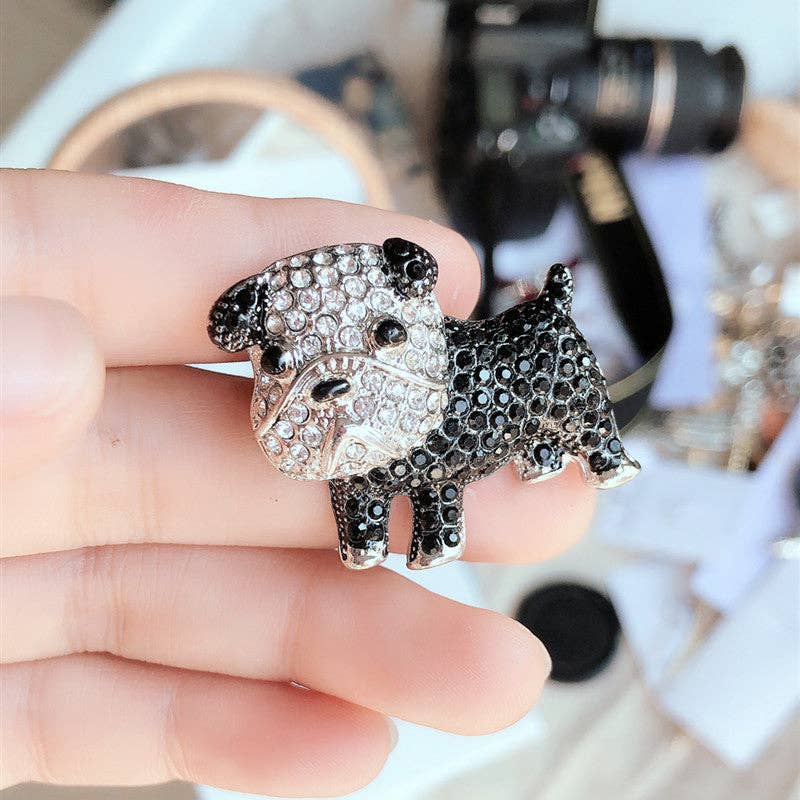 Black and silver dog-shaped brooch held by a hand with a blurred background