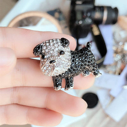 Black and silver dog-shaped brooch held by a hand with a blurred background