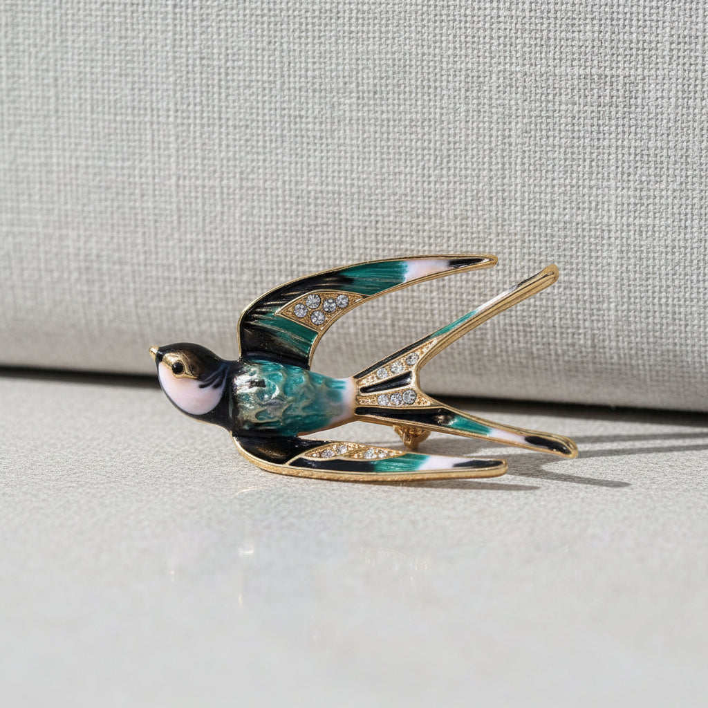 A swallow-shaped brooch with black, white, and blue enamel details and clear rhinestone accents on the wings, shown on a beige background