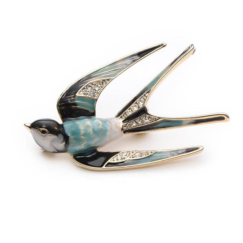 A swallow-shaped brooch with black, white, and blue enamel details and clear rhinestone accents on the wings, shown on a white background
