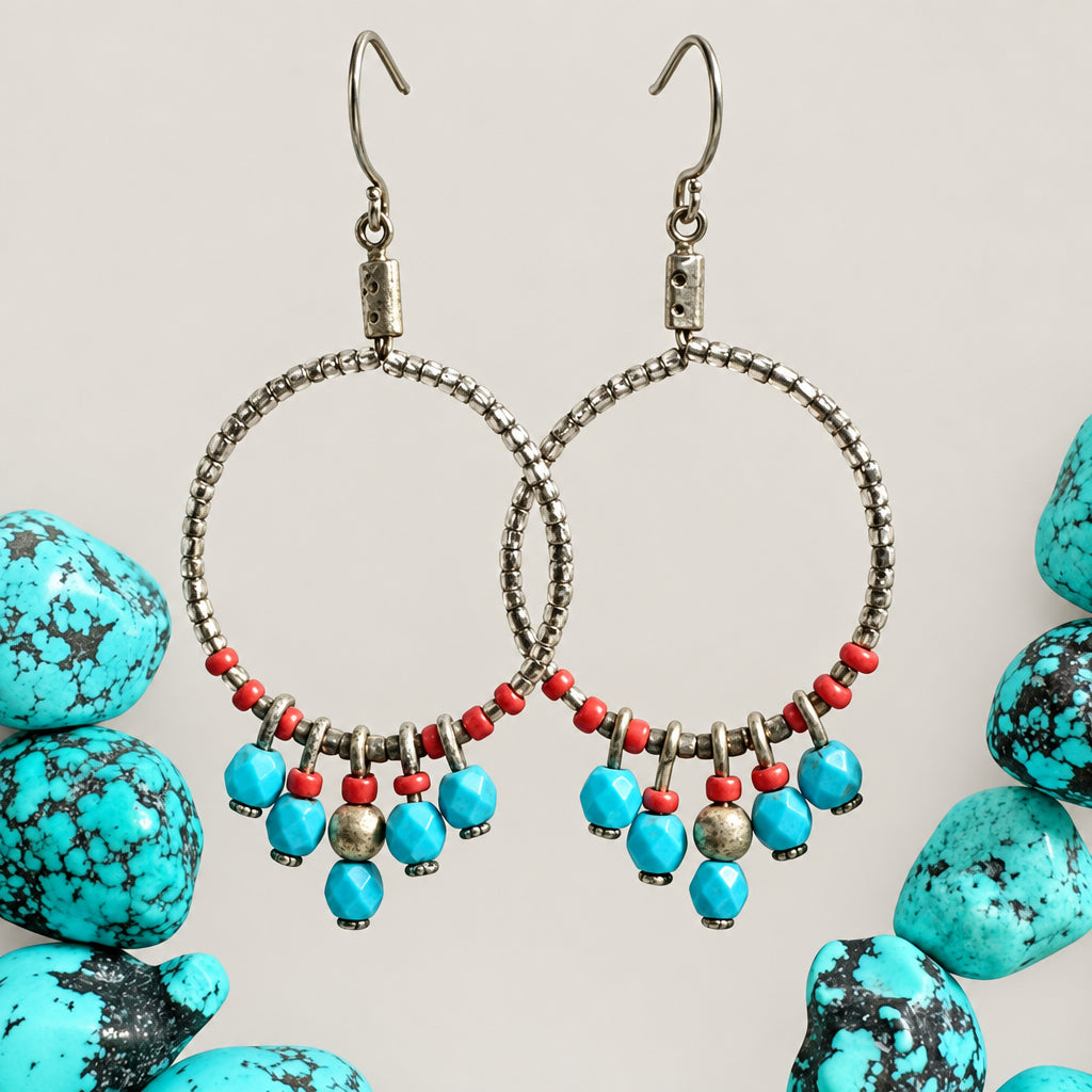 A pair of bohemian-style hoop earrings with textured silver-tone wire hoops, small red beads, and dangling turquoise-blue and gold-toned beads, displayed on a neutral background with decorative turquoise stones.