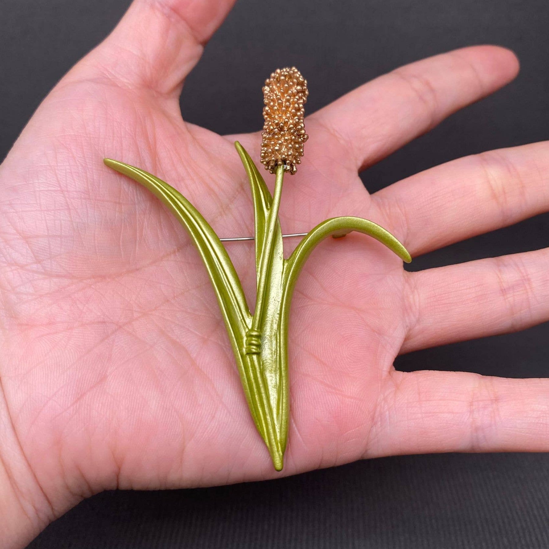 Brooch shaped like a cattail reed held in a hand