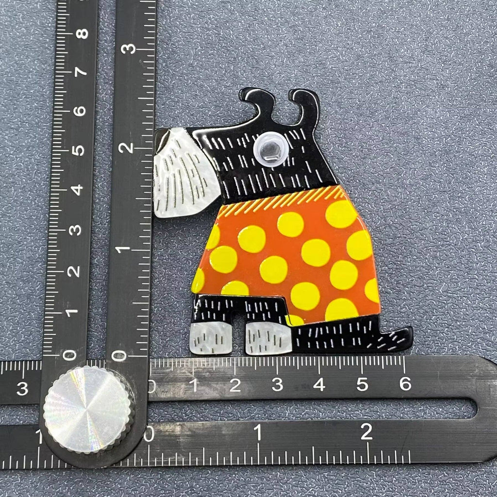 Dog-shaped brooch with black, orange, and yellow design on a gray background