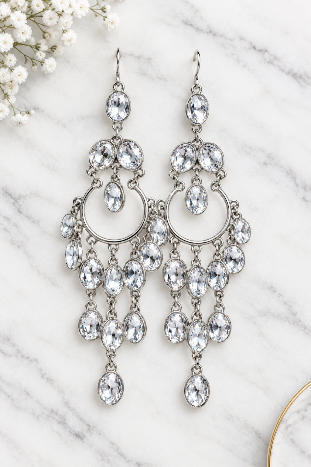 A pair of silver-toned chandelier drop earrings with multiple clear faceted rhinestones, displayed against a white marble background.