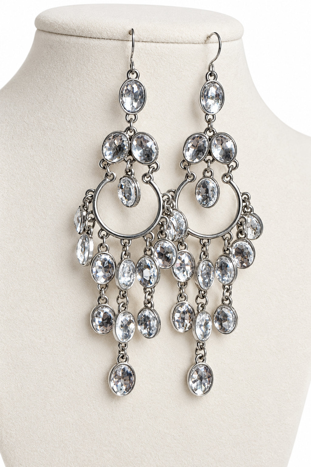 A pair of silver-toned chandelier drop earrings with multiple clear faceted rhinestones, displayed on a cream-colored jewelry bust.