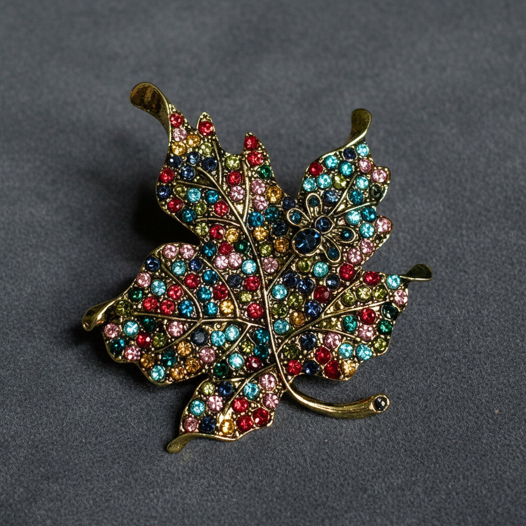 Colorful leaf-shaped brooch with gemstones on a textured blue background