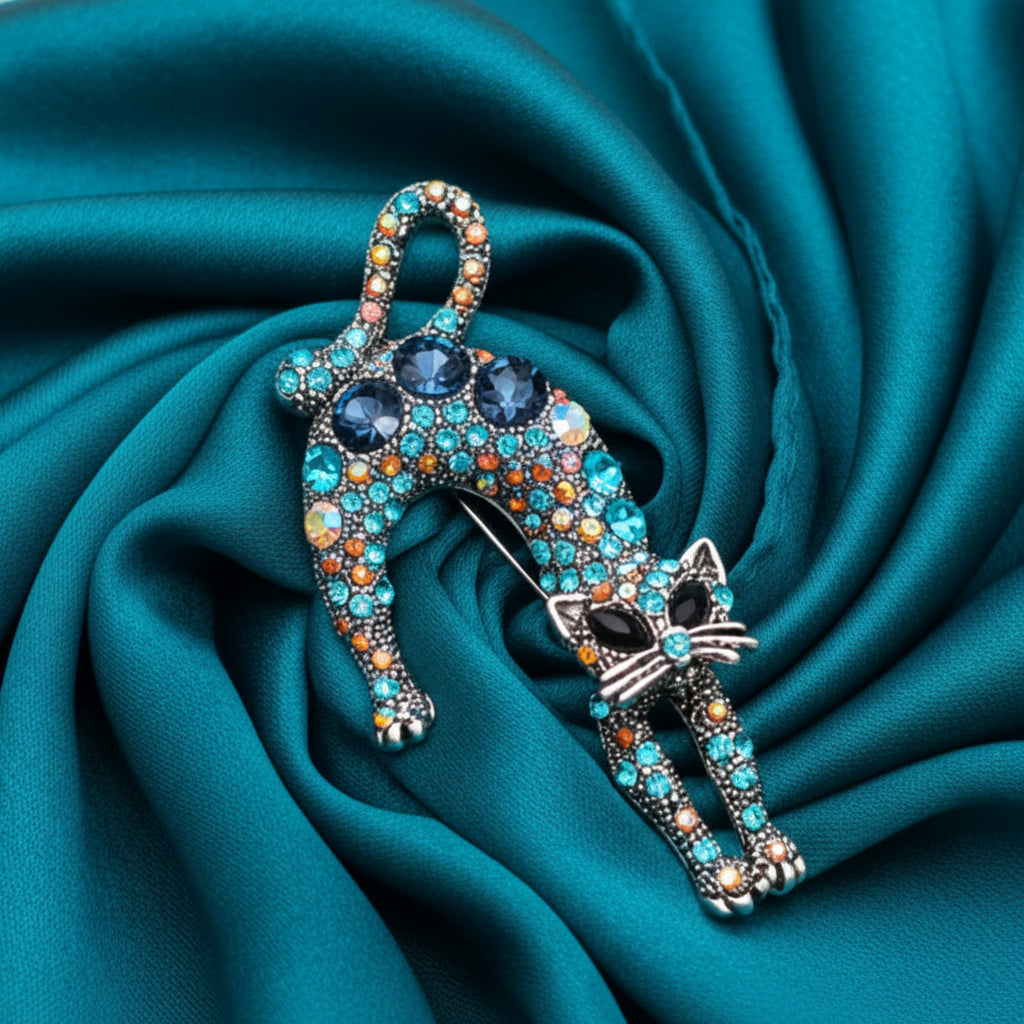Decorative cat-shaped brooch with colorful gemstones on a blue satin surface