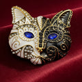 Cat-shaped mask brooch with gold, black, and white design on a red background