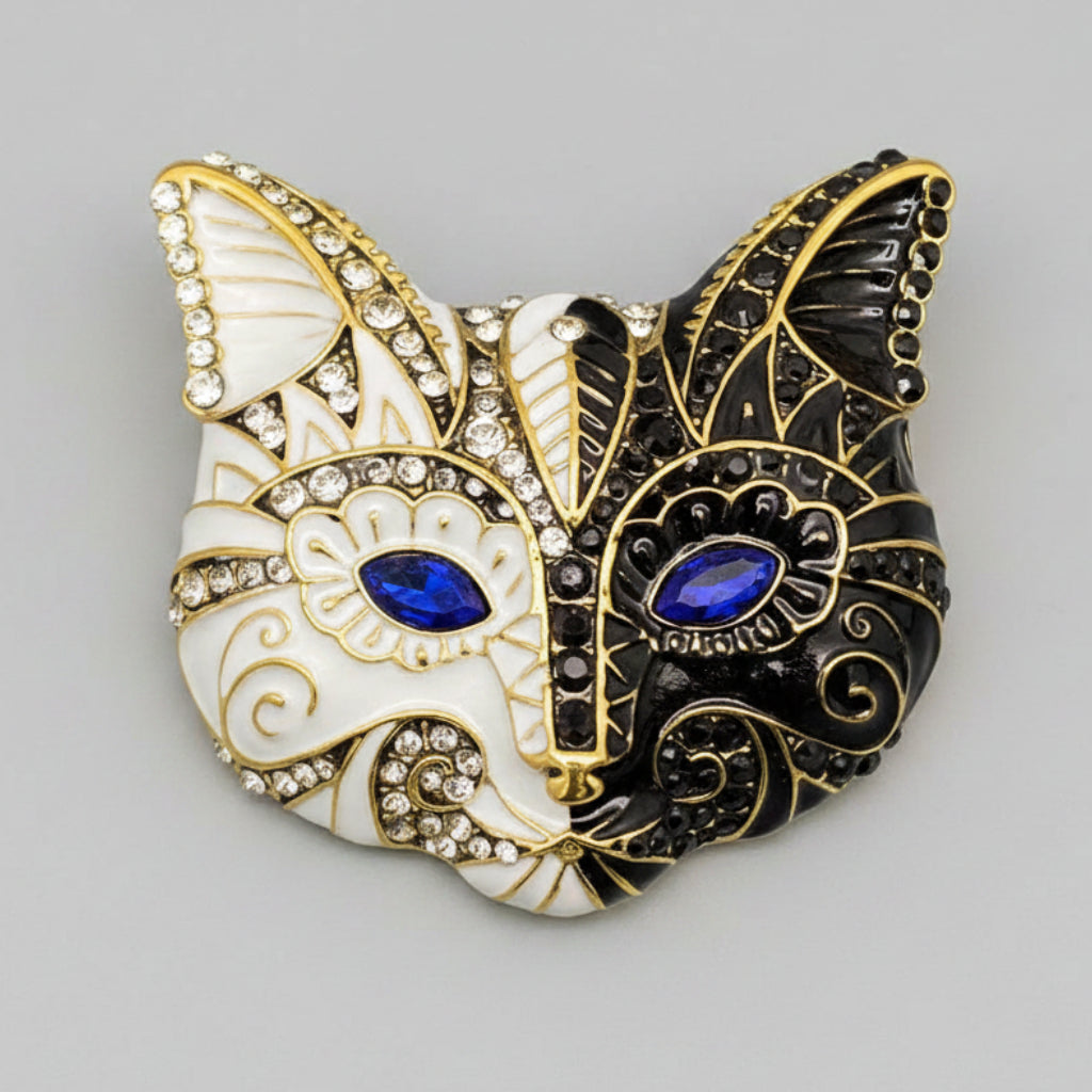 Cat-shaped mask brooch with gold, black, and white design on a gray background
