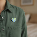 Blue and green heart-shaped earth pin pinned on a  shirt