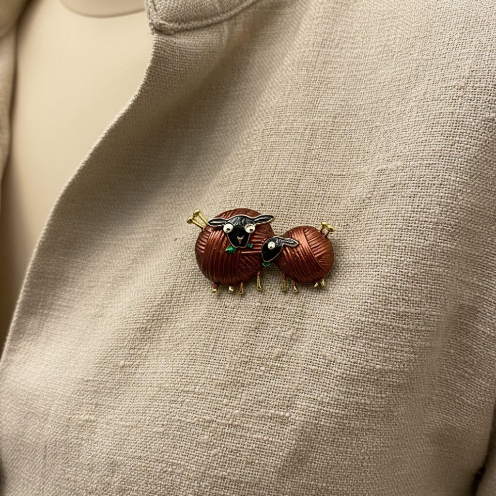 Pair of sheep-shaped brooch pins on a textured beige background