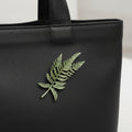 Fern leaf shape plant brooch pinned on a black leather bag