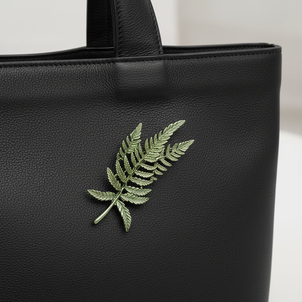 Fern leaf shape plant brooch pinned on a black leather bag
