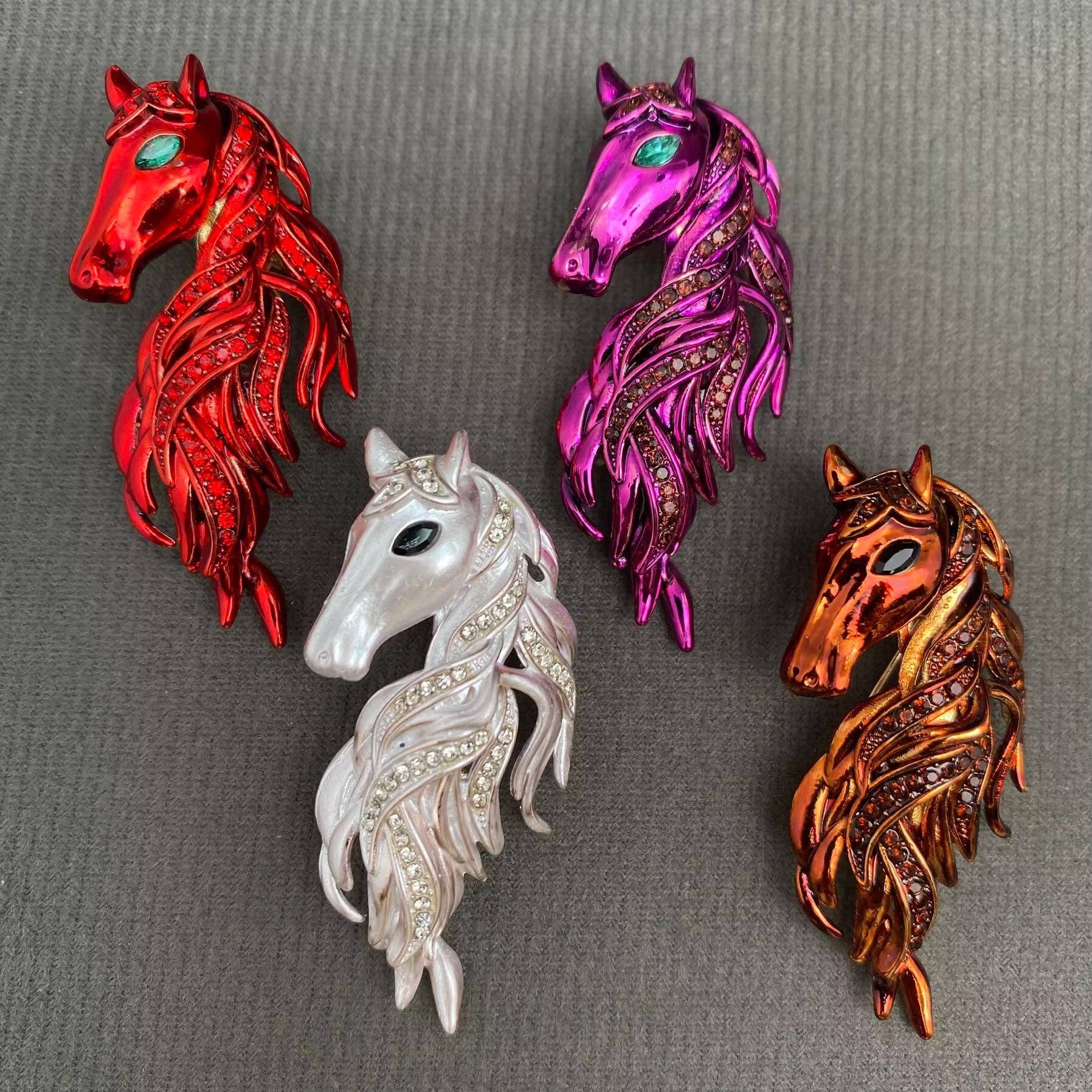 Four horse-shaped brooches in red, purple, white, and bronze on a gray background