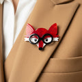 Red fox-shaped brooch with black glasses pinned on a beige suite