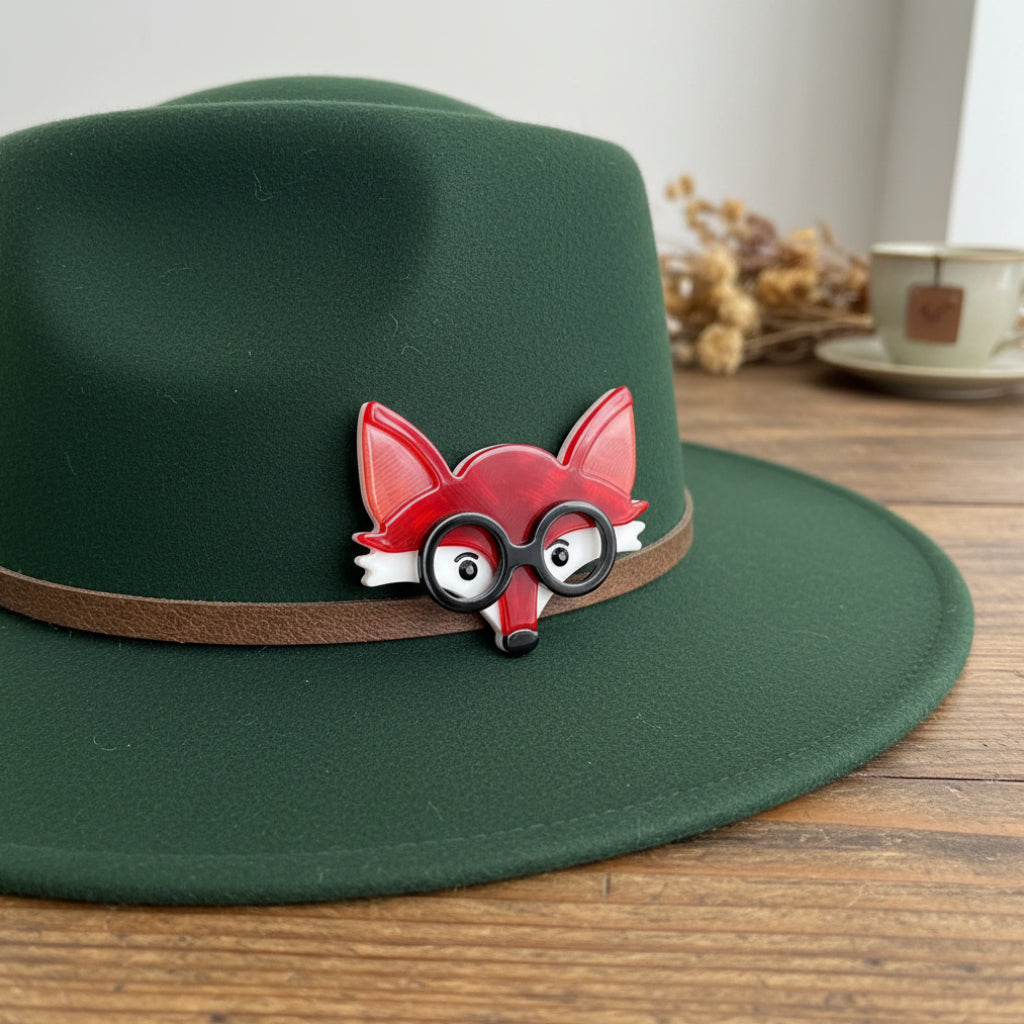 Red fox-shaped brooch with black glasses pinned on a green hat