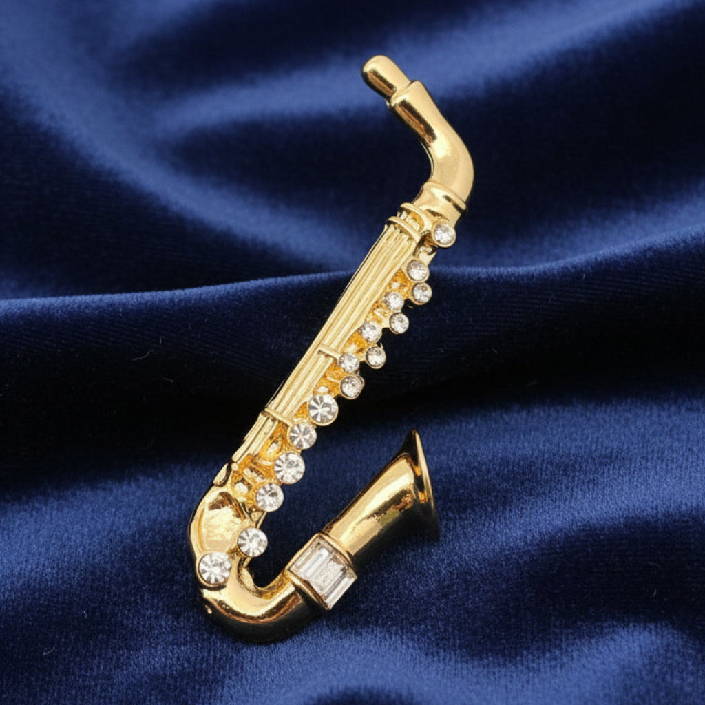 Gold saxophone-shaped brooch with rhinestones on a blue velvet background 