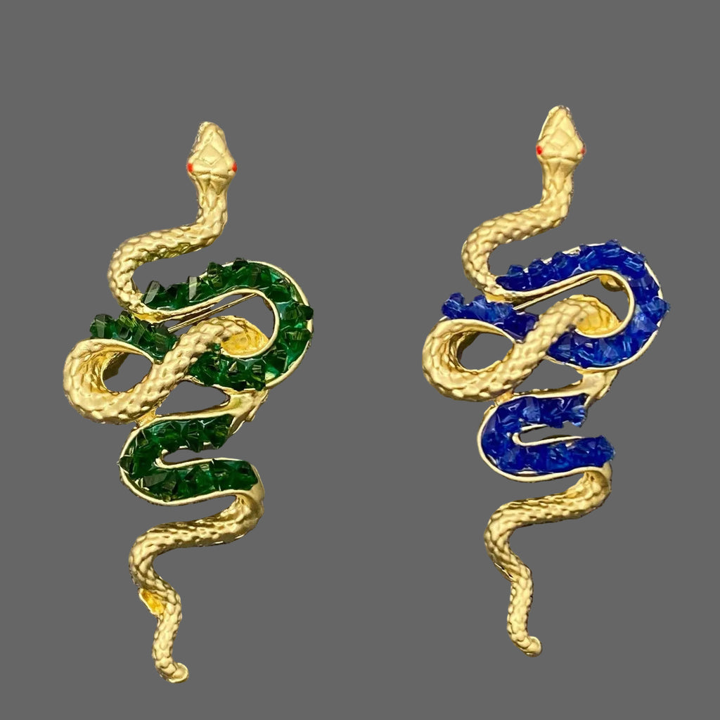 Pair of snake-shaped brooch pins  with green and blue accents on a textured gray background
