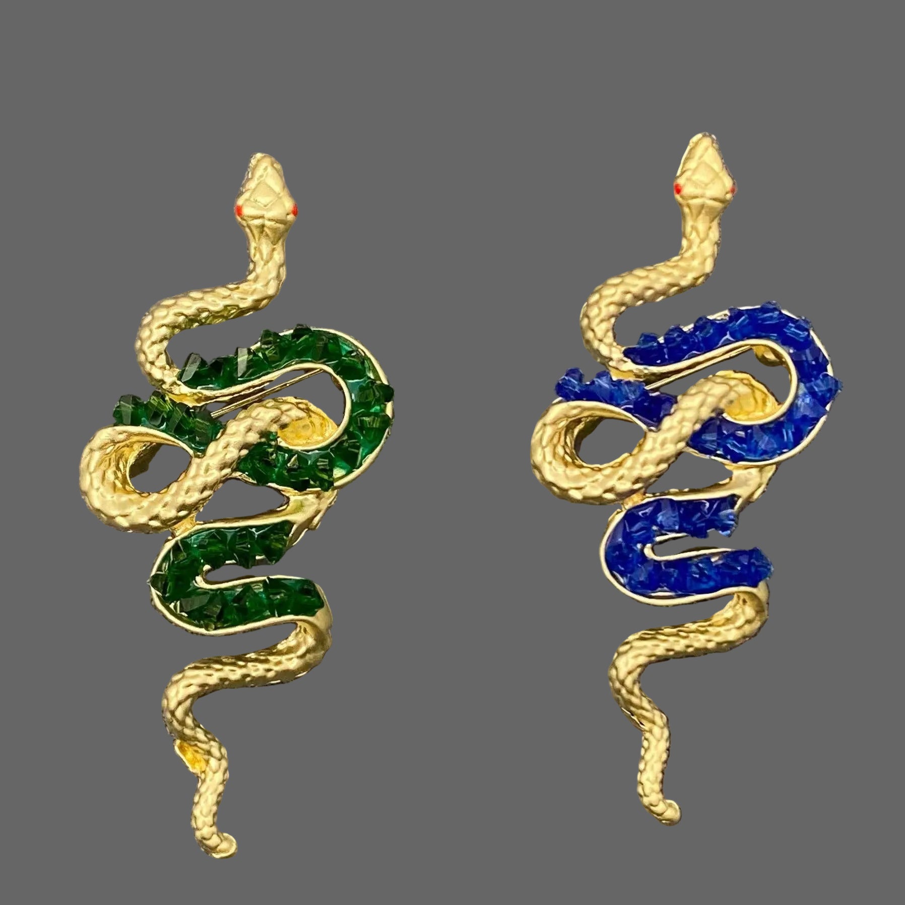 Pair of snake-shaped brooch pins  with green and blue accents on a textured gray background