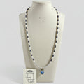 A freshwater pearl beaded necklace displayed on a cream fabric mannequin bust. The necklace features alternating strands of white pearls and dark navy blue pearls, with a central blue faceted crystal pendant.