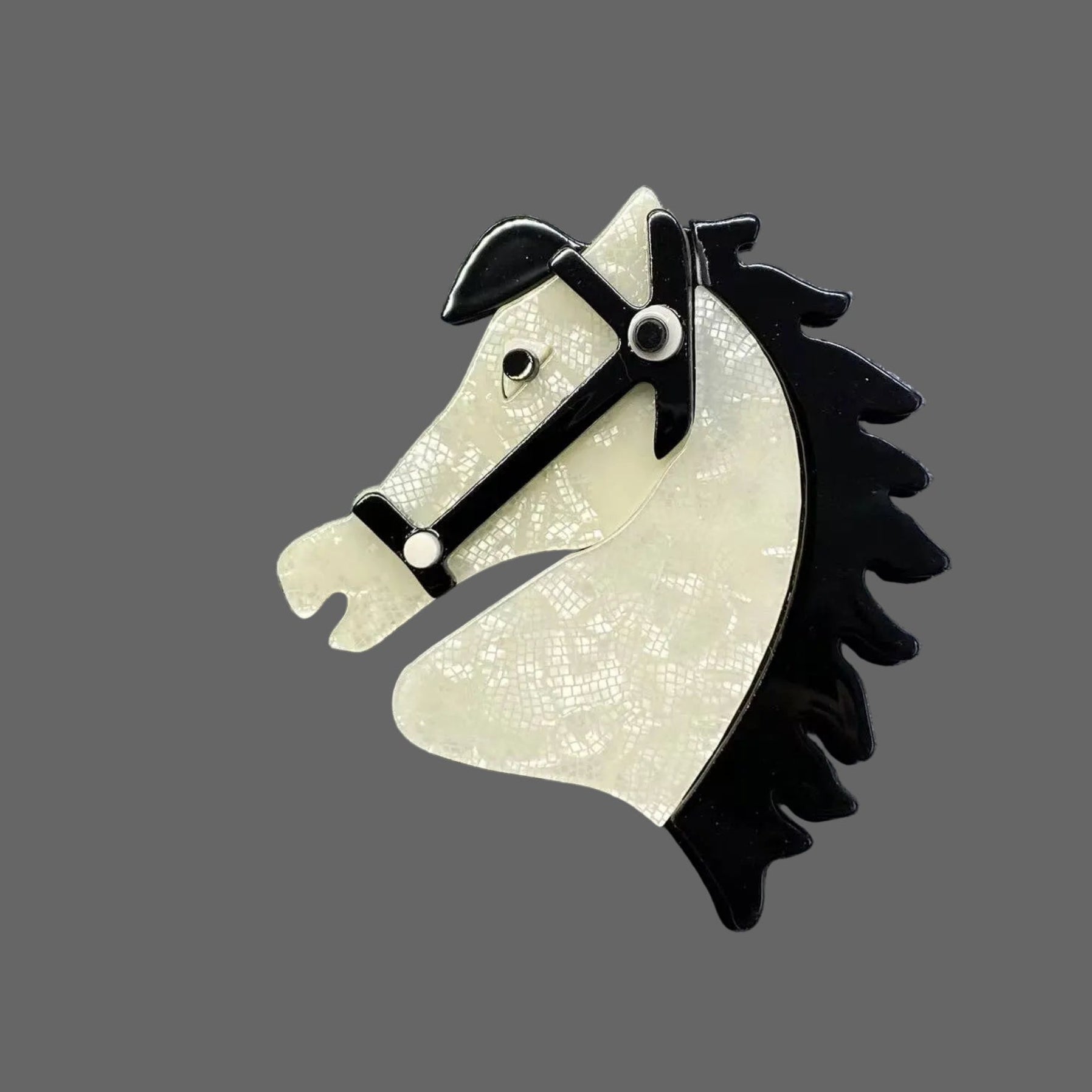 White acrylic horse head brooch with black mane on a gray background